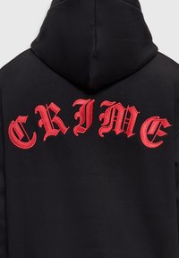 Sweat à capuche noir avec un grand texte gothique rouge brodé "CRIME" sur le haut du dos, juste en dessous de la capuche.