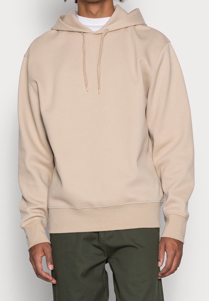 Sudadera beige con capucha hecha de tela suave, que cuenta con un bolsillo canguro, capucha con cordón y puños y dobladillo acanalados.