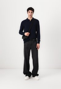 Námořnický polo svetr, černé džíny, bílé tenisky; model drží malou černou crossbody tašku; jednolitý pozadí.