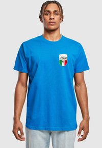 T-shirt in cotone blu con un piccolo logo a scudo colorato sul lato sinistro del petto con del testo. Maniche corte e scollo rotondo, vestibilità comoda.