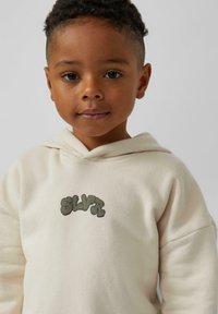 Lichtbeige hoodie met "SLVR" in donkergroene letters, gemaakt van een zachte, gestructureerde stof met een ontspannen pasvorm en een voorkant kangaroo zak.