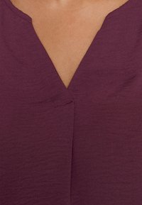 Haut violeta à col en V présentant une texture subtile, avec une couture centrale au niveau de l'encolure, créant une silhouette épurée et simple.