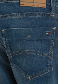 Tummansinisiä farkkuja, joissa on takatasku, jossa on erottuva ommel ja pieni logo-tunnus punaisella, valkoisella ja sinisellä.