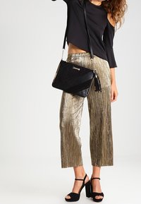 Svart handväska med fransdetalj, matchad med en svart off-the-shoulder topp och metallisk guldvida byxor. Klacksandaler fulländar outfiten.