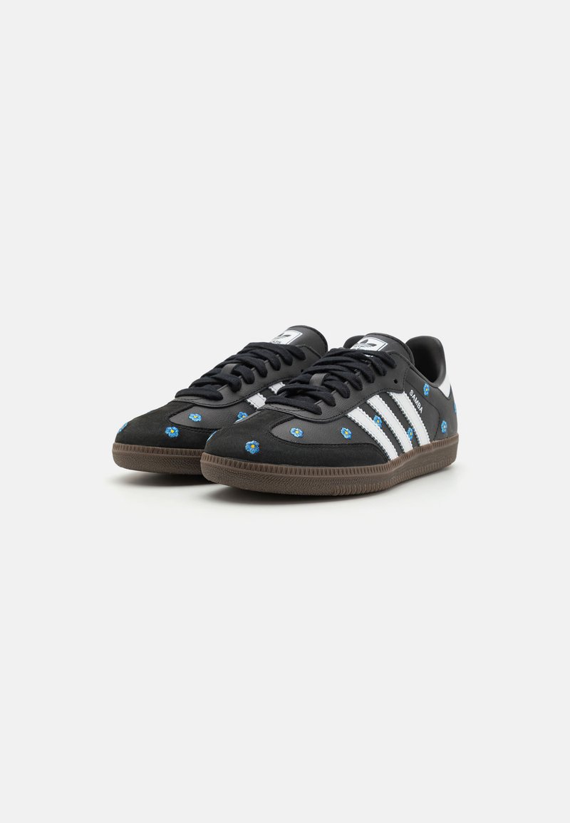 Zapatillas negras con rayas blancas y bordado floral. Cuenta con una suela de goma y un diseño de cordones. Parte superior de ante texturizado y sintético.