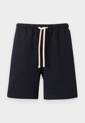 Mustad elastse vöökohaga lühikesed püksid beeži paelaga, põlvini, pehmest kangast, ühtlase hele tausta ees.