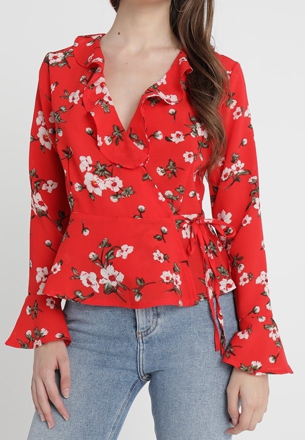 Femme portant un chemisier cache-cœur à fleurs rouge avec un col à volants et des manches évasées, associé à un jean bleu clair.