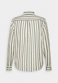 Chemise à manches longues avec boutons et motif rayé vertical noir et blanc, vue de dos sur un fond clair uni.