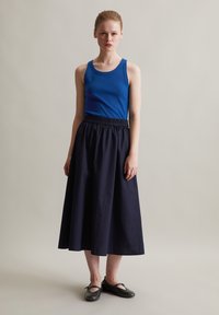 Niebieski top na ramiączkach, ciemnonavy spódnica z elastycznym pasem, czarne płaskie buty. Spódnica ma gładką teksturę, natomiast top jest dopasowany i lekko elastyczny.