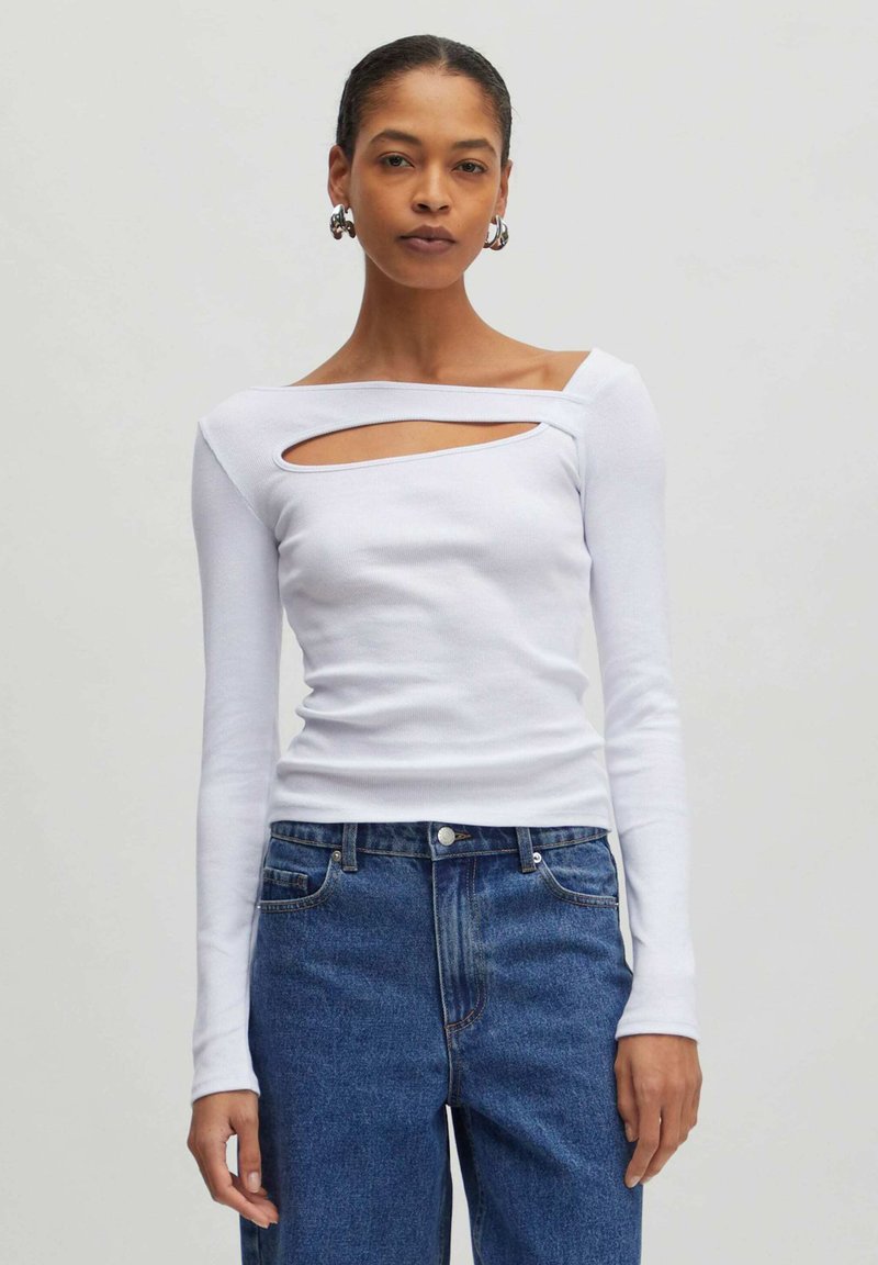 Weißes Langarmoberteil mit Ausschnitt und quadratischem Ausschnitt, kombiniert mit hoch taillierten blauen Jeans. Glatte Stofftextur.