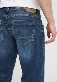 Mørkeblå denimjeans med en falmet finish, med baklommer som har dekorative sømmer og en skinnlogo på linningen.
