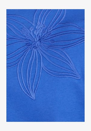 Blauer Stoff mit geprägtem Blumendesign. Die Blume hat detaillierte Blütenblätter und einen strukturierten Mittelpunkt, wodurch ein Relief-Effekt auf der Oberfläche entsteht.