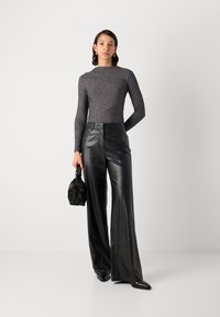 Pantalons en cuir noir à jambes larges associés à un haut à manches longues en tricot côtelé foncé avec un design diagonal. Les accessoires comprennent un petit sac noir.