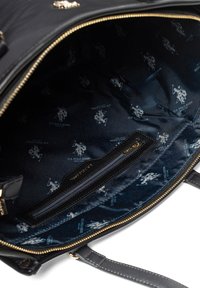 Czarna podszewka torby z kieszenią na zamek błyskawiczny; wzór powtarzającego się logo w niebieskim i białym kolorze; gładka faktura materiału. Widoczne złote detale zamka.