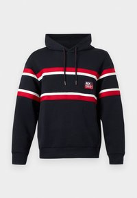 Sudadera marino con franjas horizontales rojas, blancas y negras. Presenta un bolsillo frontal, capucha con cordones y un parche con el logo en el pecho.