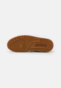 Semelle d'une basket Jordan marron avec des motifs de grip texturés et le mot Jordan embossé près du talon sur un fond blanc.