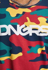 Tricou din bumbac multicolor, cu un model camuflaj în verde, galben, roșu și bleumarin, având un logo îndrăzneț „DNGRS” expus proeminent.