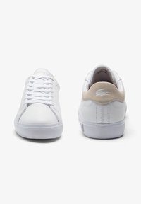 Bílé kožené tenisky s bílými tkaničkami, jemným béžovým semišovým akcentem na patě, texturovanou bílou gumovou podrážkou a logem na zadní straně.