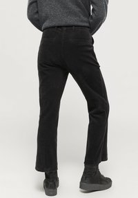 Svart kordflamsbyxor med midja på mellanhöjd och rak ben. Har bakfickor och en strukturerad tygyta. Skorna är mörka och robusta.