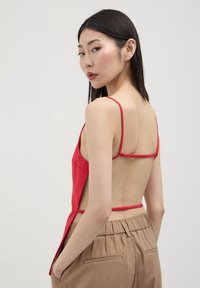 Top rosso senza maniche con spalline sottili, caratterizzato da una schiena aperta e spacchi laterali. Abbinato a pantaloni beige dalla vestibilità comoda. Tessuto a trama liscia.