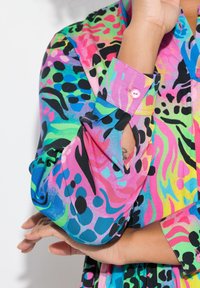 Chemise colorée avec des motifs vibrants en rose, vert, bleu et noir, dotée d'un poignet boutonné et d'une texture douce et lisse.