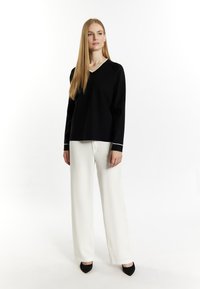 Zwarte V-halstrui met witte accenten, gecombineerd met witte wijde broek en zwarte puntige hakken, met een gladde textuur.
