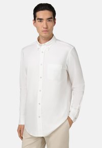 Camicia bianca con bottoni in tessuto morbido, dotata di colletto, una singola tasca sul petto e maniche lunghe con polsini abbottonati.