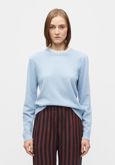 Pull bleu clair avec un col côtelé et un détail festonné, associé à un pantalon rayé verticalement rouge et noir. Texture lisse, coupe ajustée.