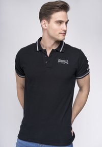 Polo negro con cuello de rayas grises, tapeta de tres botones y detalles de logo. Fabricado con tela texturizada, diseño ajustado, mangas cortas.