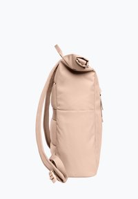 Beige rugzak met een zachte textuur, een oprol sluiting, een gevoerde body en één verstelbare schouderband, met een zijvak en minimale hardware.