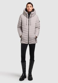 Puffjakke i lys grå med høj krave, lynlåslukning og justerbar hætte. Har et quiltet design og sidelommer.
