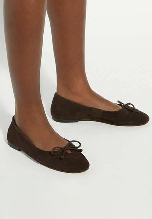 Brown suede ballet flats with a rounded toe, small bow detail on the front, and a flat sole, showcasing a smooth texture.