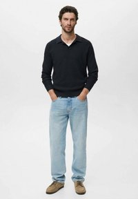 Camisa negra de manga larga con textura acanalada, jeans rectos de color azul claro y zapatos color beige. Cuello simple, corte relajado y tonos neutros.
