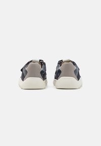 Baksidevisning av sneakers som har en kombinasjon av marineblå og lysegrå materialer, teksturerte detaljer og en hvit gummisåle.