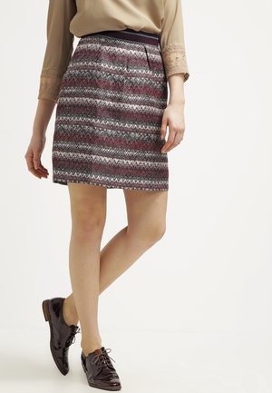 Una gonna con motivo a zigzag nei colori bordeaux, grigio e bianco, con una vita aderente e una texture morbida. Abbinata a scarpe lucide.