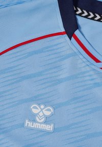 Lichtblauw sportshirt met een textuurpatroon, rode accenten en een marineblauwe kraag. Hummel-logo in het wit onderaan geplaatst.