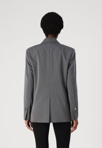 Gray tailored blazer featuring long sleeves, a notched collar, and a single vent detail at the back. Silver hardware accents on cuffs.