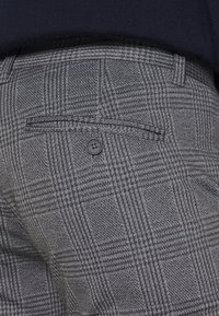 Grijze geruite broek met een subtiel ruitpatroon, zijzak met knoopsluiting en een gestructureerde stofafwerking.