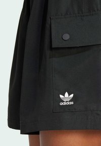 Pantalones cortos negros hechos de tela ligera con un bolsillo frontal, cierre de broche y el logo blanco de Adidas en la parte inferior izquierda.