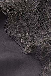 Mørkt stof med indviklet blonderdetaljer med blomsterdesign, bølgede kanter og en glat tekstur over det hele.