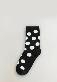 Czarna bawełniana skarpetka w białe kropki. Posiada prążkowany ściągacz i bezszwowy palec dla wygody. Standardowa długość ściągająca.