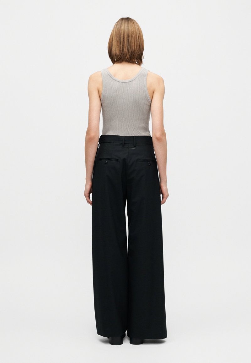 Débardeur gris côtelé et pantalon large noir à texture lisse, avec deux poches arrière et une taille haute.