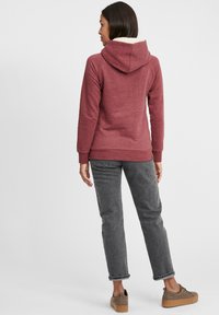 Felpa in pile bordeaux con cappuccio, foderata in bianco e con polsini a costine, abbinata a jeans grigi a gamba dritta e scarpe piattaforma marroni con un upper decorato.