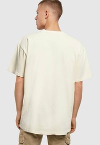Krémová oversized tričko vyrobené z mäkkého bavlneného materiálu, s krátkymi rukávmi a klasickým okrúhlym výstrihom, zobrazené zozadu.