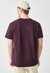 Bordo bavlněné tričko s klasickým kulatým výstřihem, krátkými rukávy a volným střihem. Obsahuje švy podél spodního lemu a výstřihu.