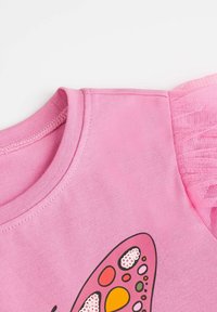 Różowa bawełniana koszulka z nadrukiem motyla, z fakturowanymi różowymi falbanami z tiulu na ramionach oraz okrągłym dekoltem.