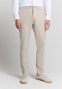 Beige broek van lichtgewicht stof met een rechte pijp, voorzien van een knoopsluiting en een slank ontwerp. Gepaard met lichtgekleurde sneakers.