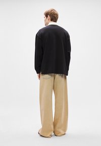 Μαύρη φούτερ μπλούζα σε oversized στυλ με μακριά μανίκια. Χαλαρά μπεζ παντελόνια με πίσω τσέπες. Απλό υφασμάτινο σχέδιο. Μινιμαλιστικός σχεδιασμός.