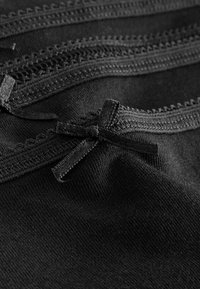 Czarna tkanina z delikatnym koronkowym wykończeniem i małymi kokardkami, ukazująca miękką fakturę z misternym haftem wzdłuż krawędzi.