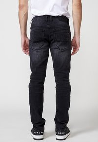 Jeans slim fit negros con bolsillos traseros, detalles de costura sutiles y una cinturilla cómoda. Llevados con zapatillas negras y blancas.
